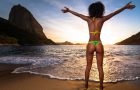Sexy Brazilian Girl in Bikini Stands in the Beach With Open Arms and Welcomes A New Day in Rio de Janeiro With the Sugarloaf Mountain in the Background